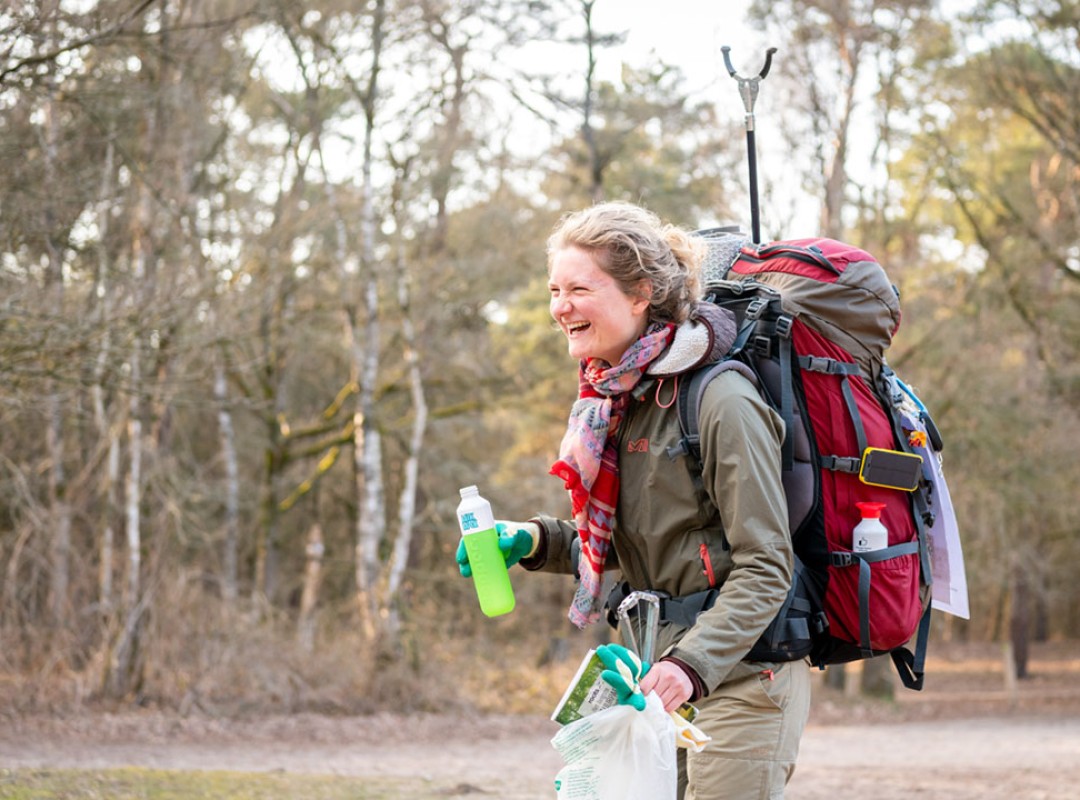 Hedwig Fossen lachend in het bos met haar rugzak en een mikmak fles