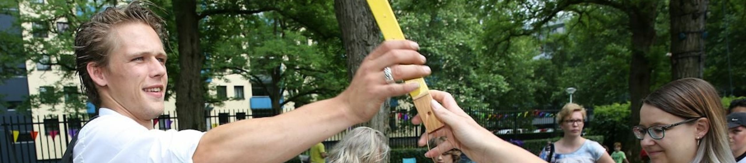 Markt met mensen, man geeft stuk hout aan ander persoon.