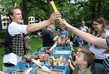 Markt met mensen, man geeft stuk hout aan ander persoon.
