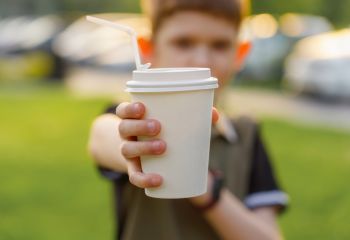 Jongetje steekt zijn hand met een wegwerpbekert uit naar de camera