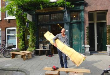 Rob de Looff buiten zijn atelier met hout in zijn hand