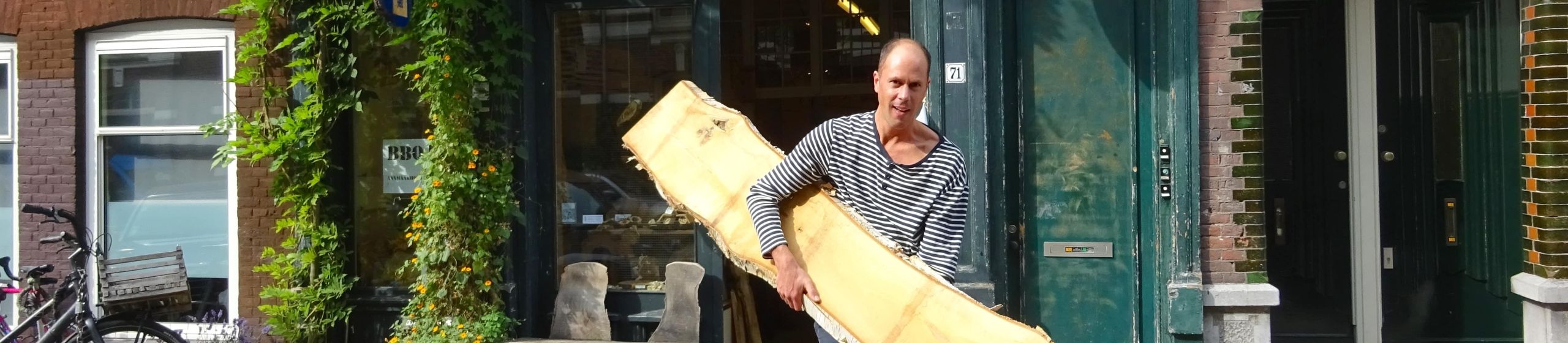 Rob de Looff buiten zijn atelier met hout in zijn hand